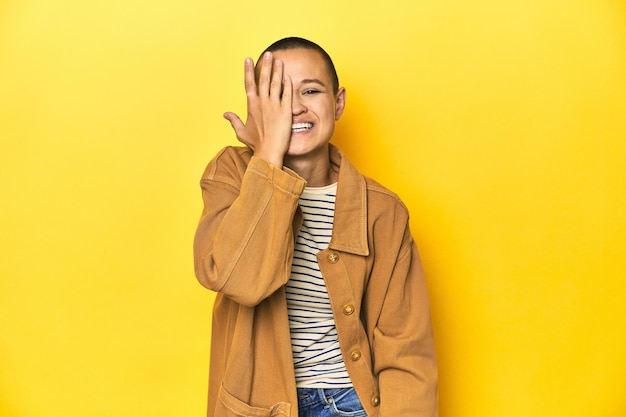 Mujer con camiseta a rayas y camisa vaquera con fondo amarillo divirtiéndose cubriendo la mitad de la cara con la palma