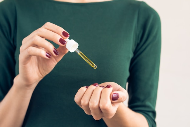 Foto mujer en una camiseta verde y una manicura marrón aplica aceite para las uñas