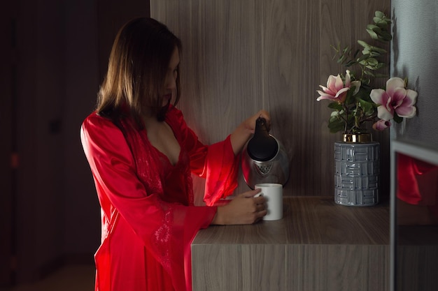 Una mujer con un camisón de satén rojo echando agua caliente por la noche.