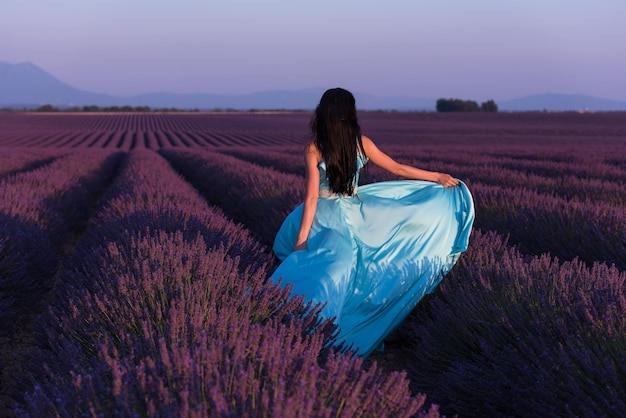 Mujer de campo de flores de lavanda en cyand vestido divirtiéndose y relajarse en el viento en el campo de flores de color púrpura