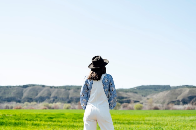 Mujer en el campo con sombrero negro en la espalda