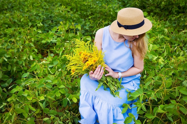 mujer en un campo verde se sienta con un ramo de flores silvestres