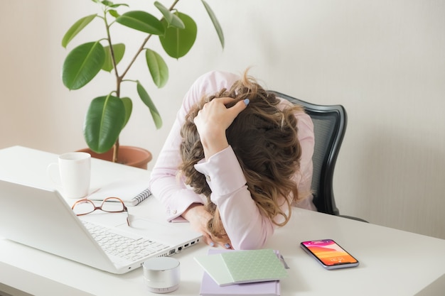 La mujer cansada apoyó la cabeza sobre la mesa. Mujer cansada con dolor de cabeza mientras estaba sentado en su lugar de trabajo en la oficina. Empresaria con exceso de trabajo. Mujer joven frustrada que mantiene los ojos cerrados