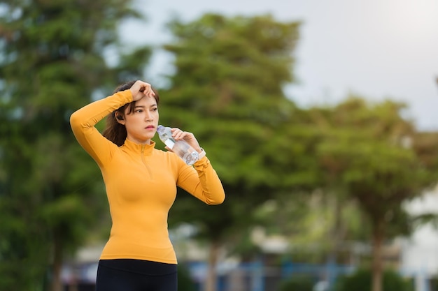 Mujer cansada bebiendo agua después de correr en el parque