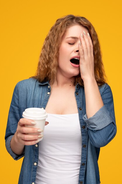 Mujer cansada con café para ir bostezando