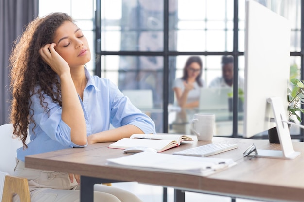 Mujer cansada con exceso de trabajo descansando mientras trabajaba en la computadora Los colegas están en el fondo