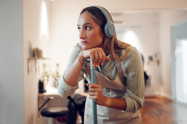 Mujer cansada y limpiando con auriculares para escuchar música mientras trabaja en la habitación de la casa Limpiadora pensando y contemplando mientras escucha un podcast de radio o una canción para descansar en el trabajo exhausto y agotado