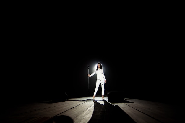 Mujer cantante en el escenario con fondo negro en un haz de luz blanca.