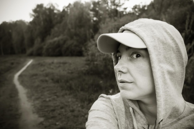 Mujer con capucha y gorra en el parque entre árboles en blanco y negro