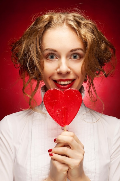 Mujer con caramelo de corazón sobre fondo rojo.