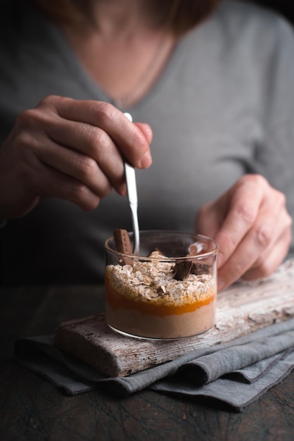 Mujer en un cardigan gris come un batido de plátano con avena vertical