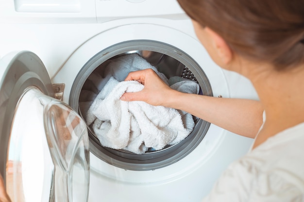 Una mujer carga ropa sucia para una lavadora.