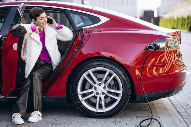 Mujer cargando auto eléctrico y hablando por teléfono