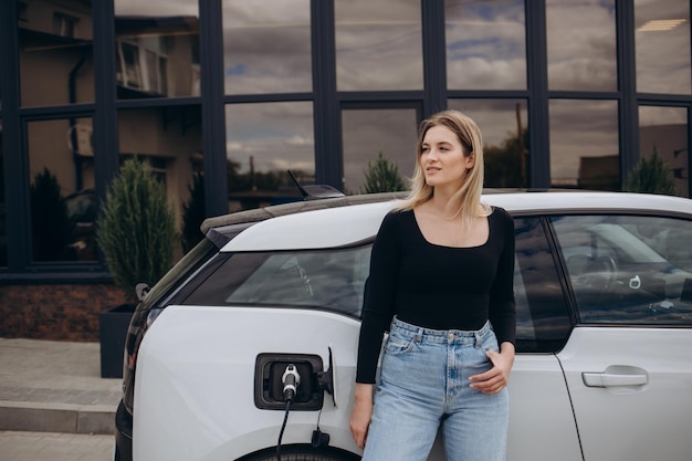 Mujer cargando electro car por su casa y sosteniendo el cargador