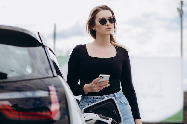 Mujer cargando electro coche en la gasolinera eléctrica