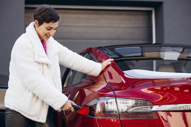 Mujer cargando electro coche con pistola de carga junto a la casa