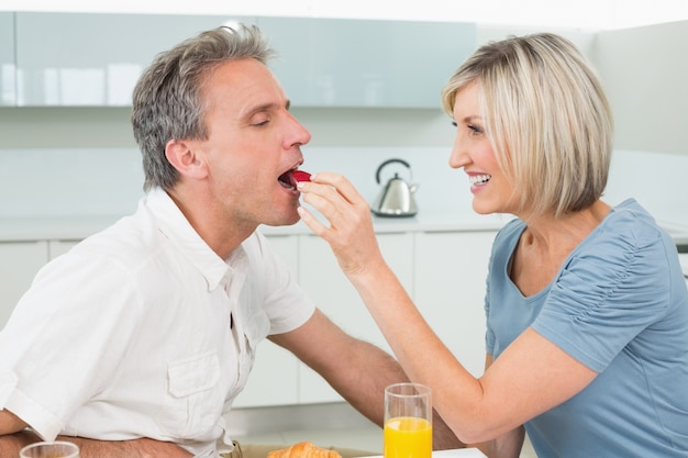 Mujer cariñosa que alimenta al hombre en la cocina