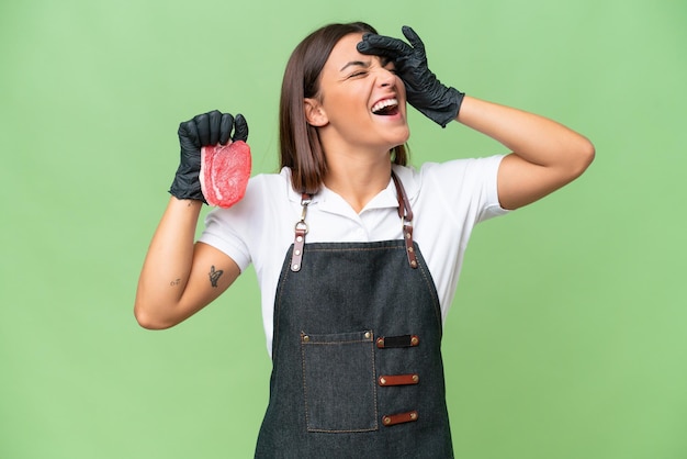 Mujer carnicera con un delantal y sirviendo carne fresca cortada aislada en un fondo de croma verde sonriendo mucho