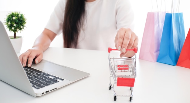 Mujer y carrito de compras pequeño con computadora portátil para el concepto de compras en línea por Internet