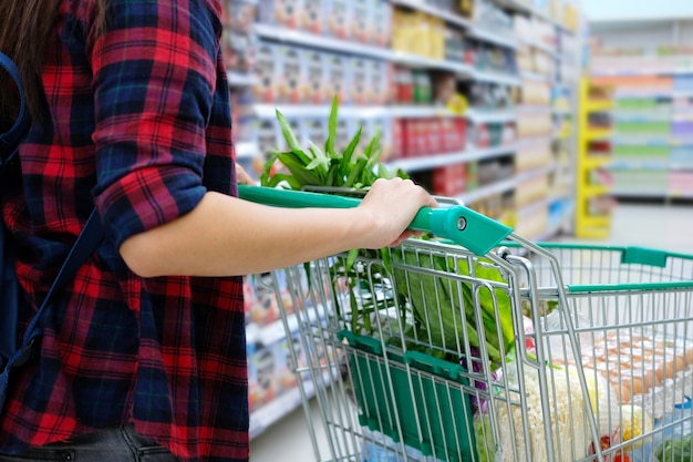 Mujer con el carro de compras que compra la comida en un supermercado.