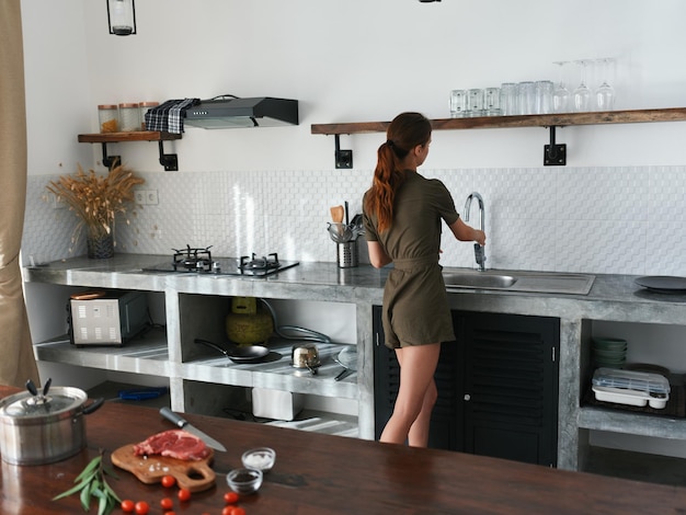 Una mujer en casa en la cocina prepara comida usando carne y verduras una cocina grande en una moderna
