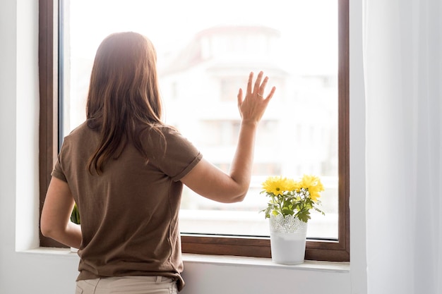 Foto mujer en casa de cuarentena mirando por la ventana