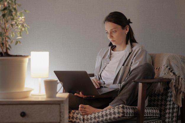 La mujer en casa está trabajando en una computadora portátil en un sillón acogedor, una mujer de negocios europea o tipos de estudiantes