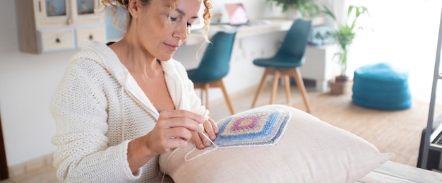 Una mujer en casa haciendo un trabajo de bordado en una almohada de decoración blanca para el pasatiempo y la actividad de ocio interior sola sentada en la mesa La vida real en el apartamento para mujeres solteras que disfrutan del tiempo