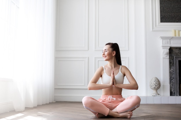 Mujer en casa en posición de loto. Retrato de joven feliz practicando yoga.