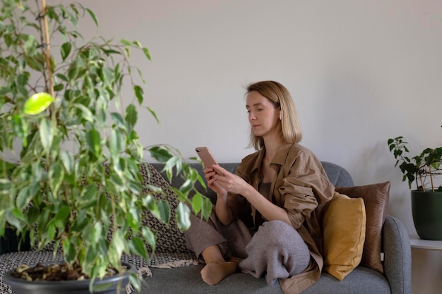 Mujer en casa usando un teléfono inteligente sentado en un sofá