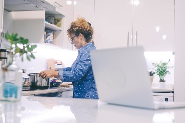 Una mujer en casa en la vida real ocupada en la cocina cocinando comida Computadora portátil en primer plano Estilo de vida de la gente moderna interior Esposa preparando el almuerzo sola en la cocina Concepto de estilo de vida de vida individual