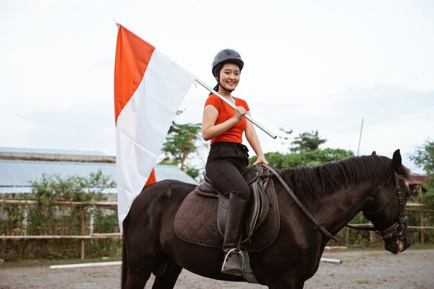 Foto mujer con casco montando un caballo con bandera indonesia