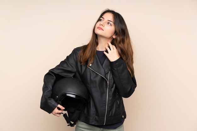 Mujer con casco de moto en pared beige pensando en una idea