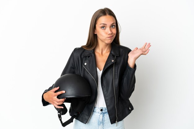 Mujer con un casco de motocicleta sobre fondo blanco aislado que tiene dudas mientras levanta las manos