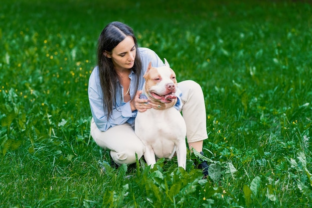 Mujer en casual acariciar american pitbull terrier sobre césped perro feliz con lengua fuera mirando a su alrededor