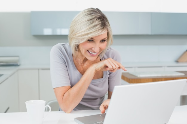 Mujer casual con café usando la computadora portátil en la cocina