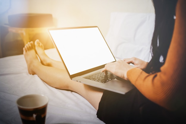 Mujer casual joven feliz que usa la computadora portátil en cama.