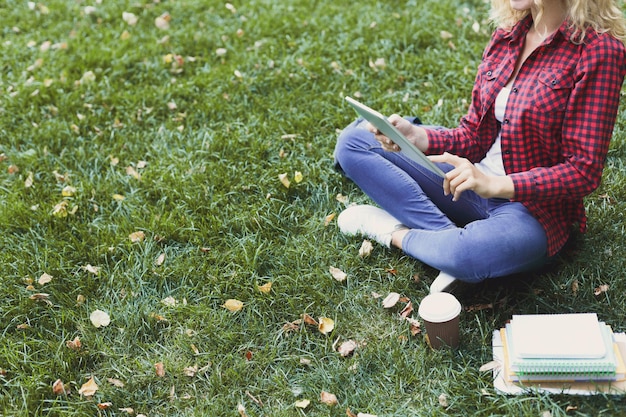 Mujer casual joven con tableta y cuadernos al aire libre. Estudiante preparándose para exámenes con libros y café en el parque. Educación e ingreso al concepto universitario, espacio de copia.