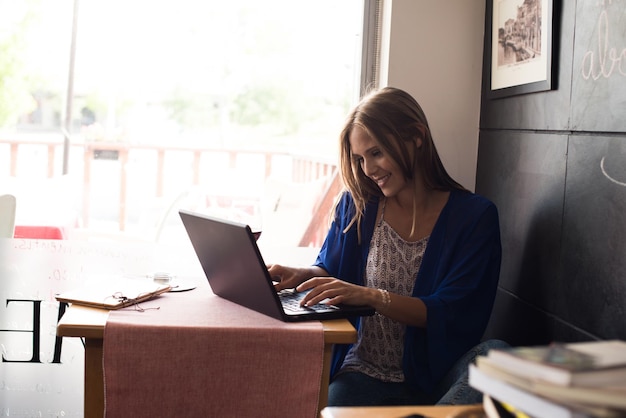 Mujer casual que usa la computadora portátil en la cafetería