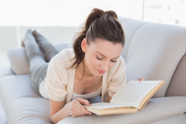 Mujer casual relajada que lee un libro en el sofá