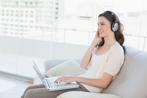 Mujer casual usando la computadora portátil mientras disfruta de la música en el sofá