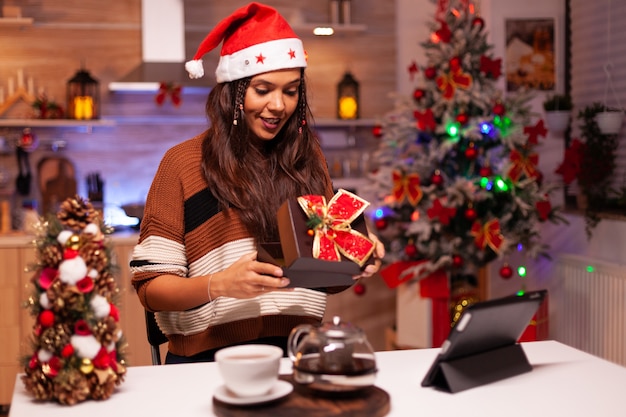 Mujer caucásica abriendo caja de regalo mientras usa videollamada