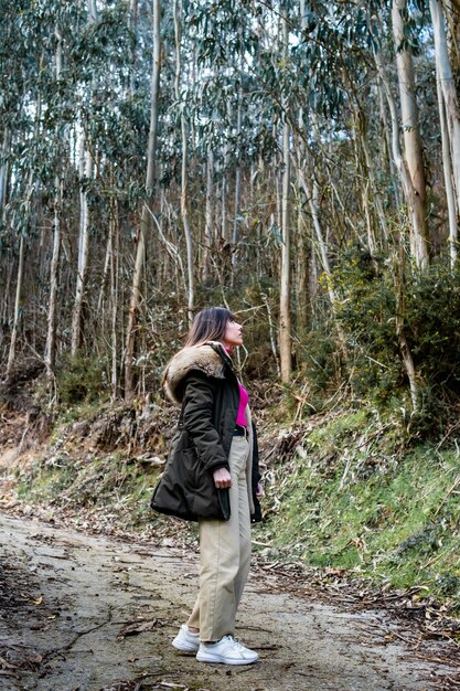 Mujer caucásica con abrigo verde y cabello castaño disfruta del ecoturismo asturiano en medio de los bosques