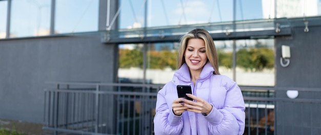 Mujer caucásica adulta mirando la pantalla del teléfono afuera con una sonrisa