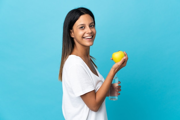 Mujer caucásica aislada en azul con una manzana y con una botella de agua