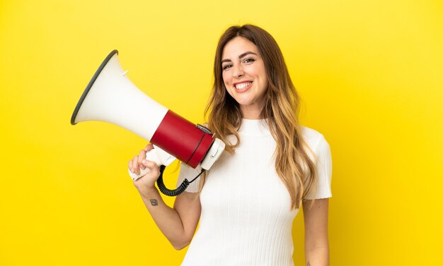 Mujer caucásica aislada sobre fondo amarillo sosteniendo un megáfono y sonriendo mucho