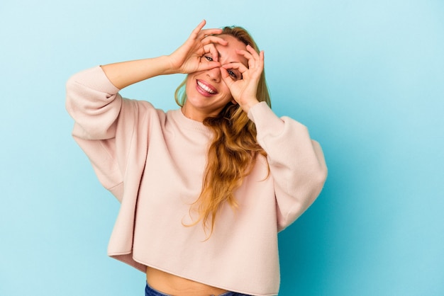 Mujer caucásica aislada sobre fondo azul mostrando bien firmar sobre los ojos