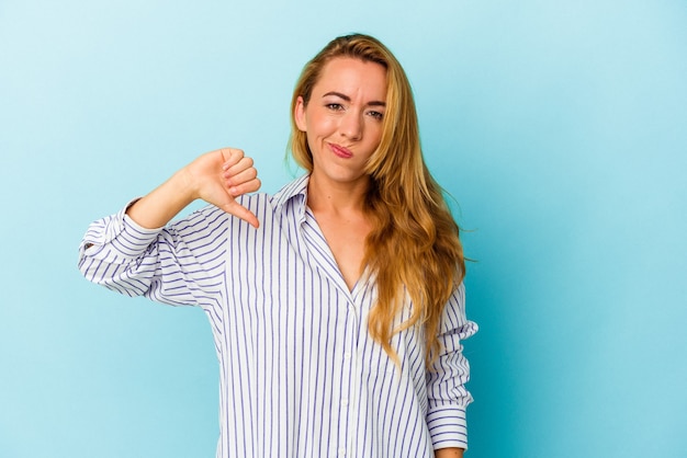 Mujer caucásica aislada sobre fondo azul mostrando el pulgar hacia abajo, concepto de decepción.