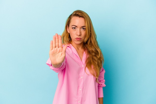 Mujer caucásica aislada sobre fondo azul de pie con la mano extendida mostrando la señal de stop, impidiéndote.