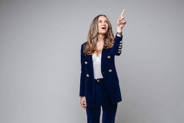 Mujer caucásica con apariencia atractiva señala algo con el dedo hacia arriba, imagen aislada en la pared gris